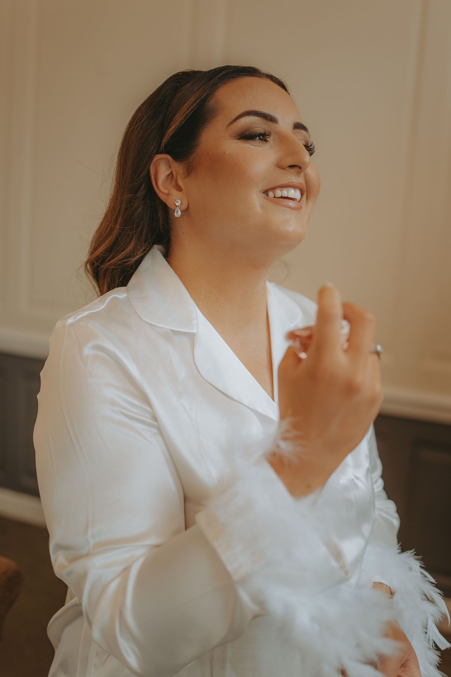 Bride wearing white satin robe with feather trim during wedding preparations.