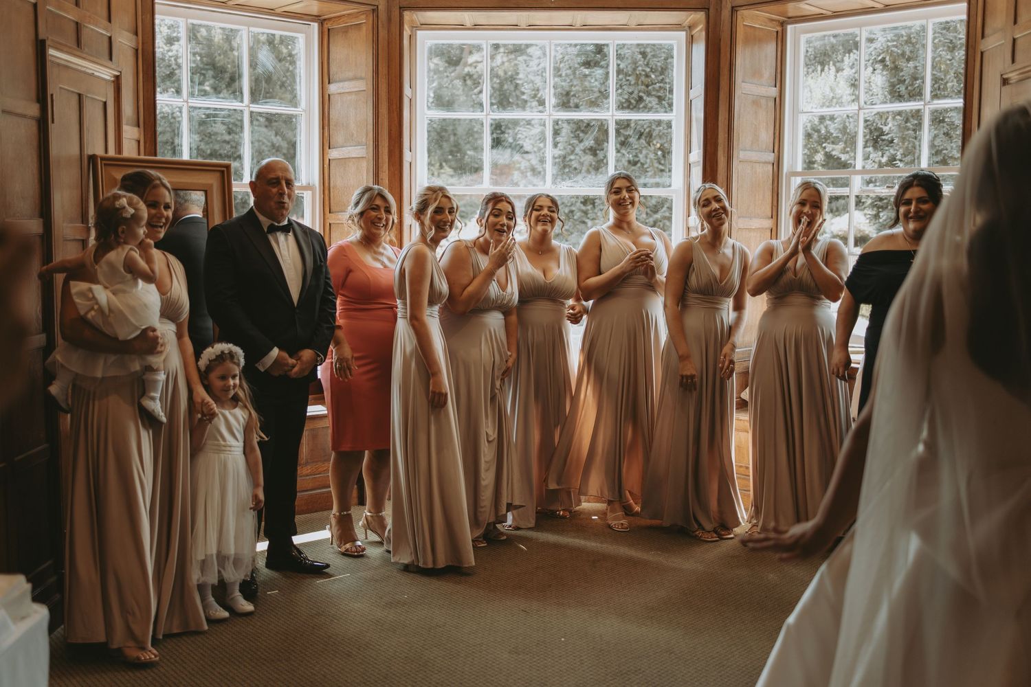 Wedding party group photo with bridesmaids in champagne dresses lined up in an elegant indoor setting.