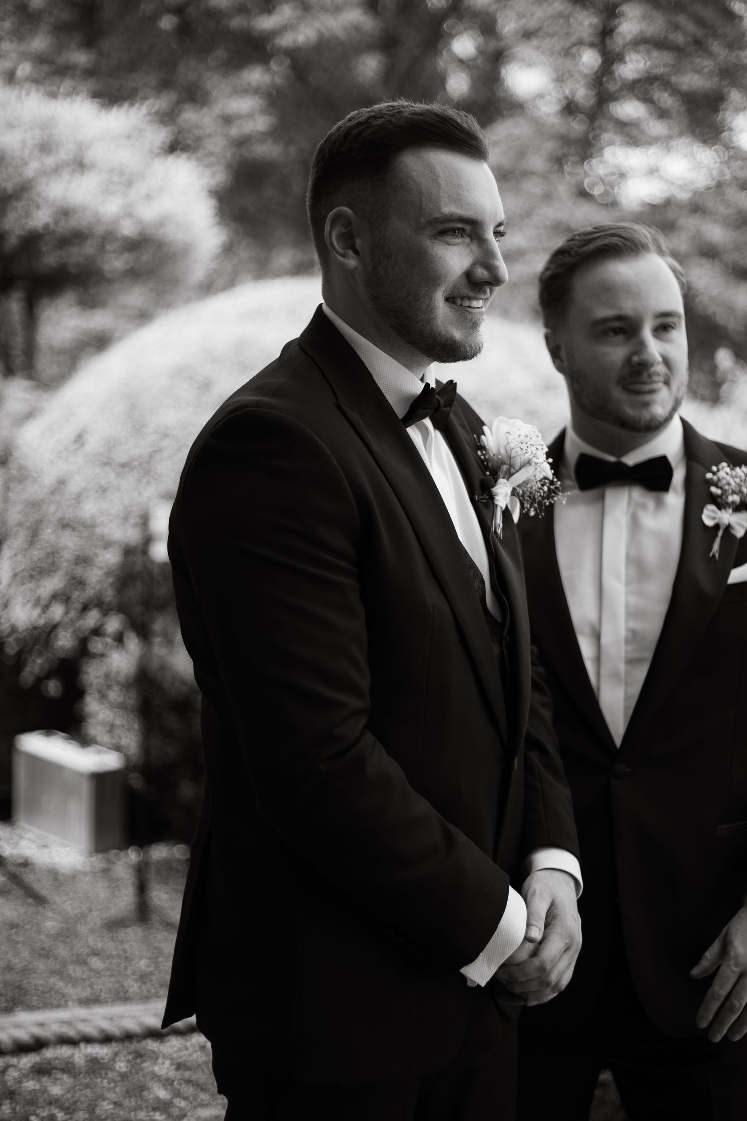 Groomsmen sharing laughs and candid moments outdoors in formal black tuxedos.