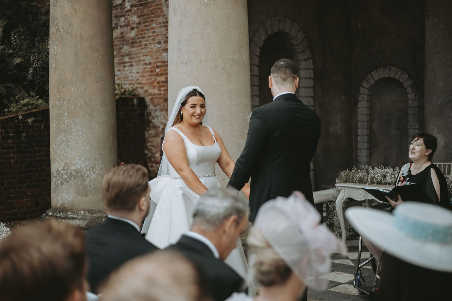Wedding ceremony takes place in a rustic brick archway setting with elegant decor and floral arrangements.