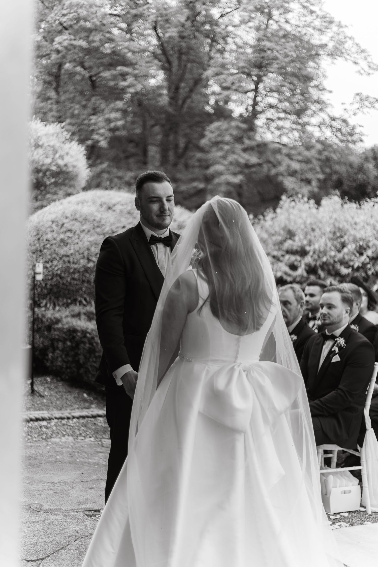 A wedding ceremony first look moment captured in black and white with guests looking on in the background.