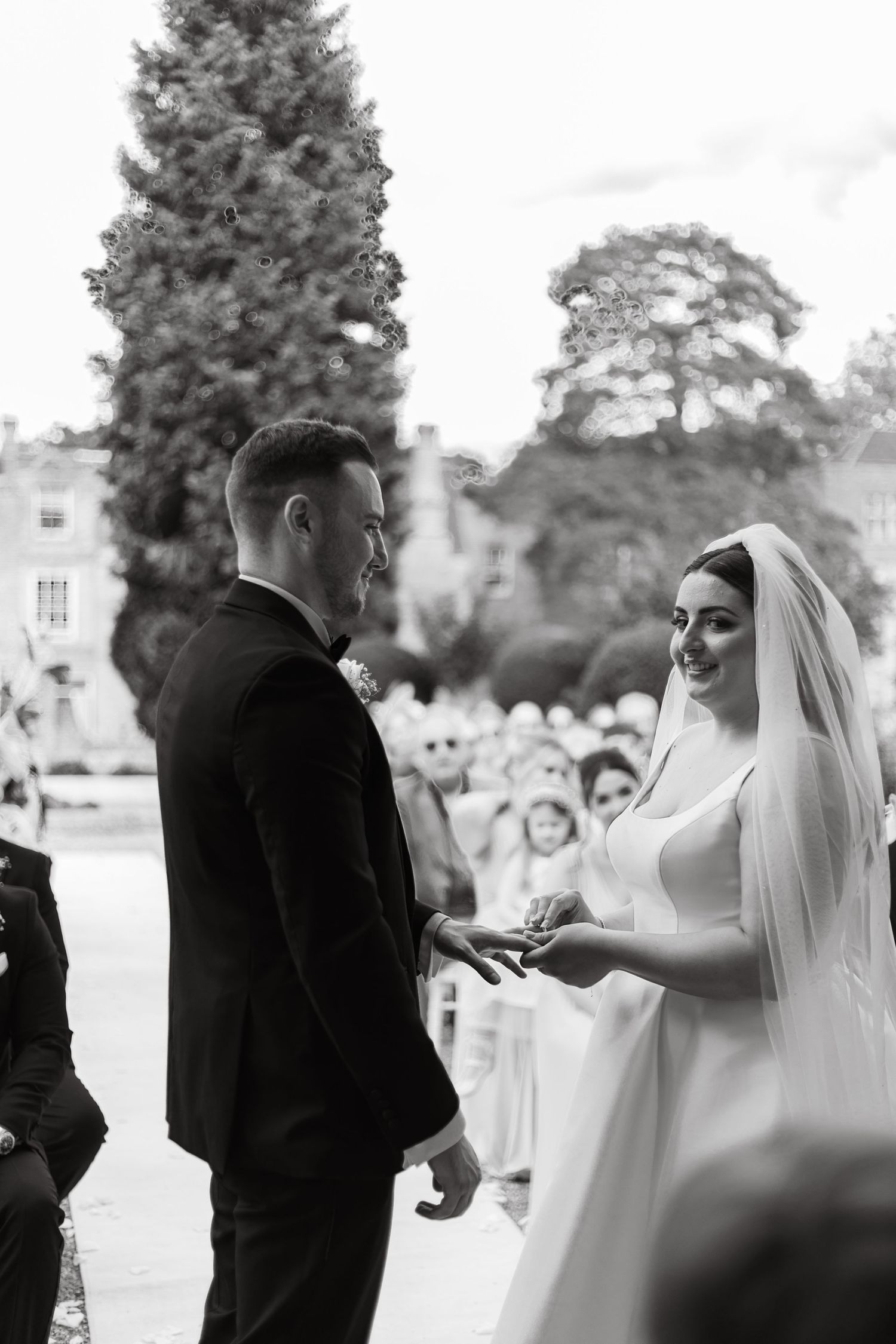 Black and white photo captures ring exchange moment during outdoor wedding ceremony.