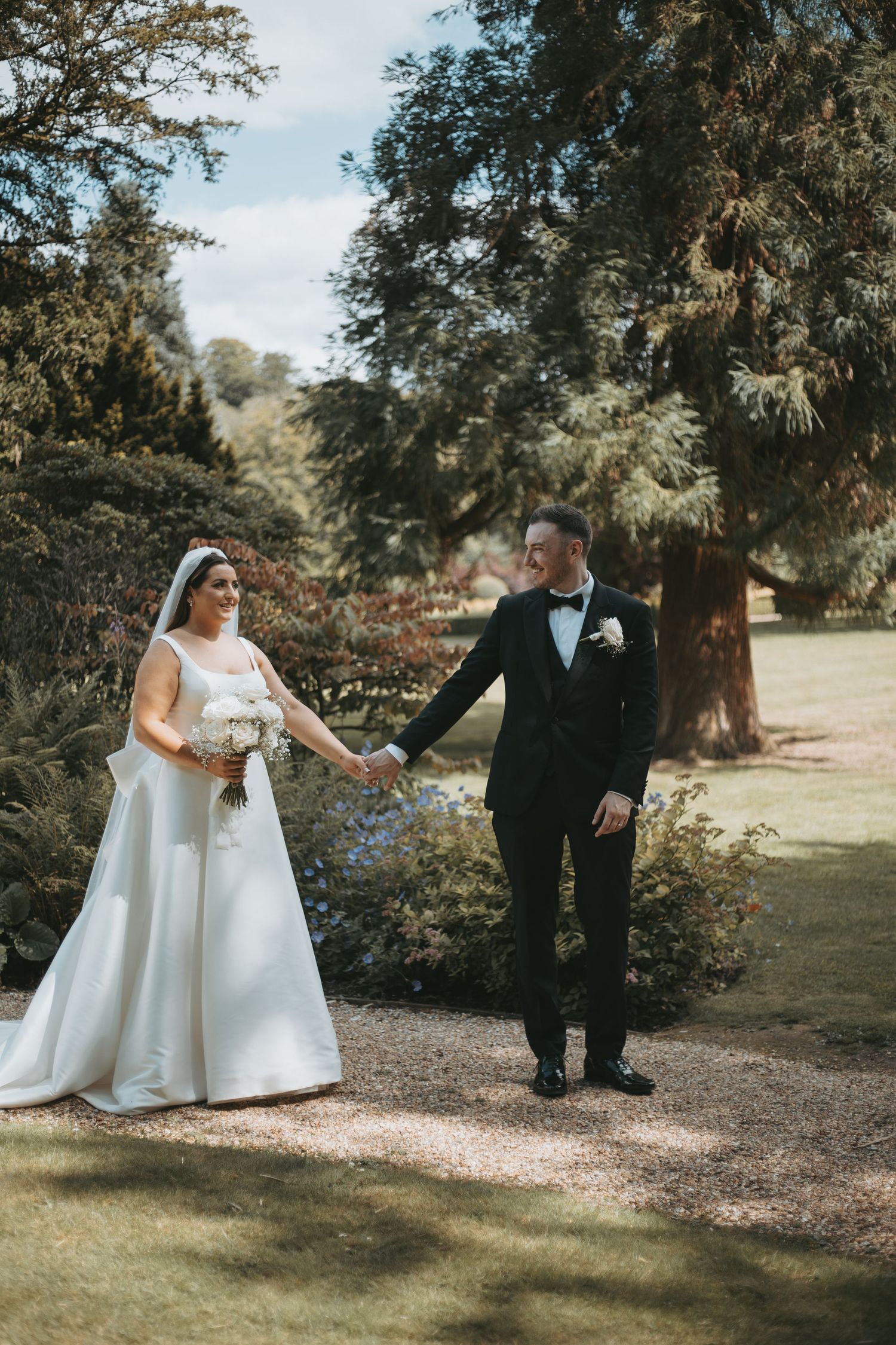 Wedding couple walking together on a garden path surrounded by lush greenery.