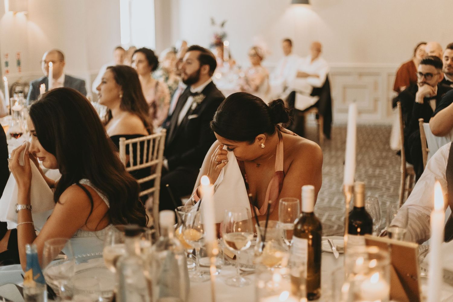 Wedding reception guests celebrate at elegantly decorated tables with glowing lights and white decor.