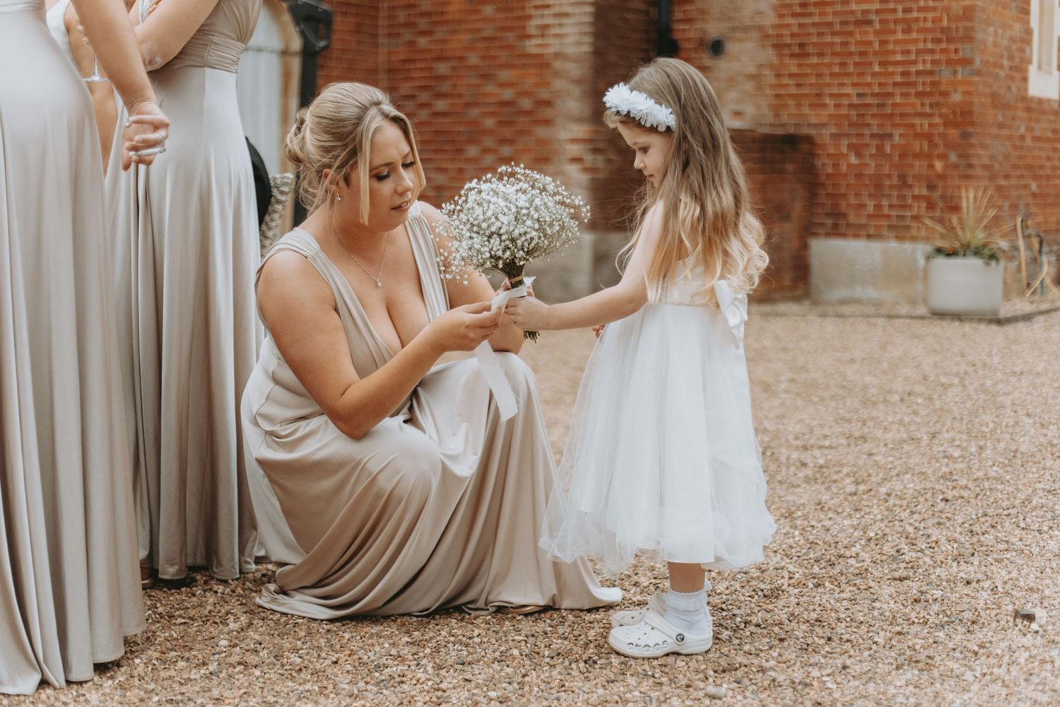 Bridesmaids in neutral dresses gather outdoors at rustic brick venue.