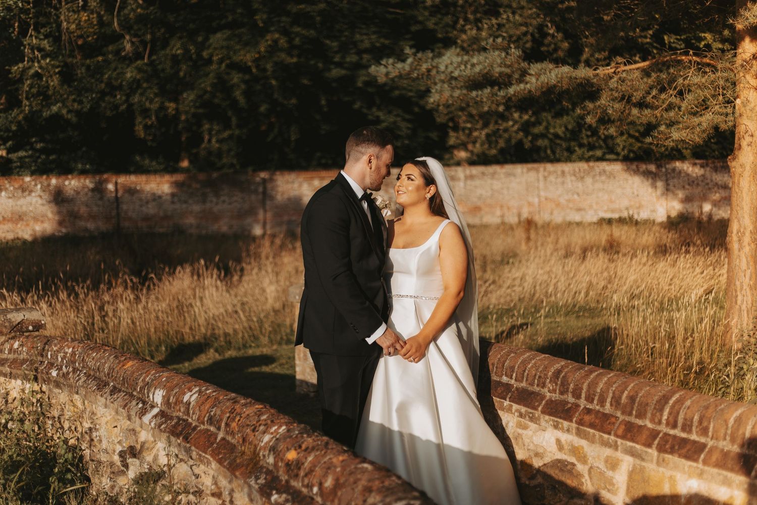 Couple poses against rustic brick wall during golden hour wedding photoshoot.