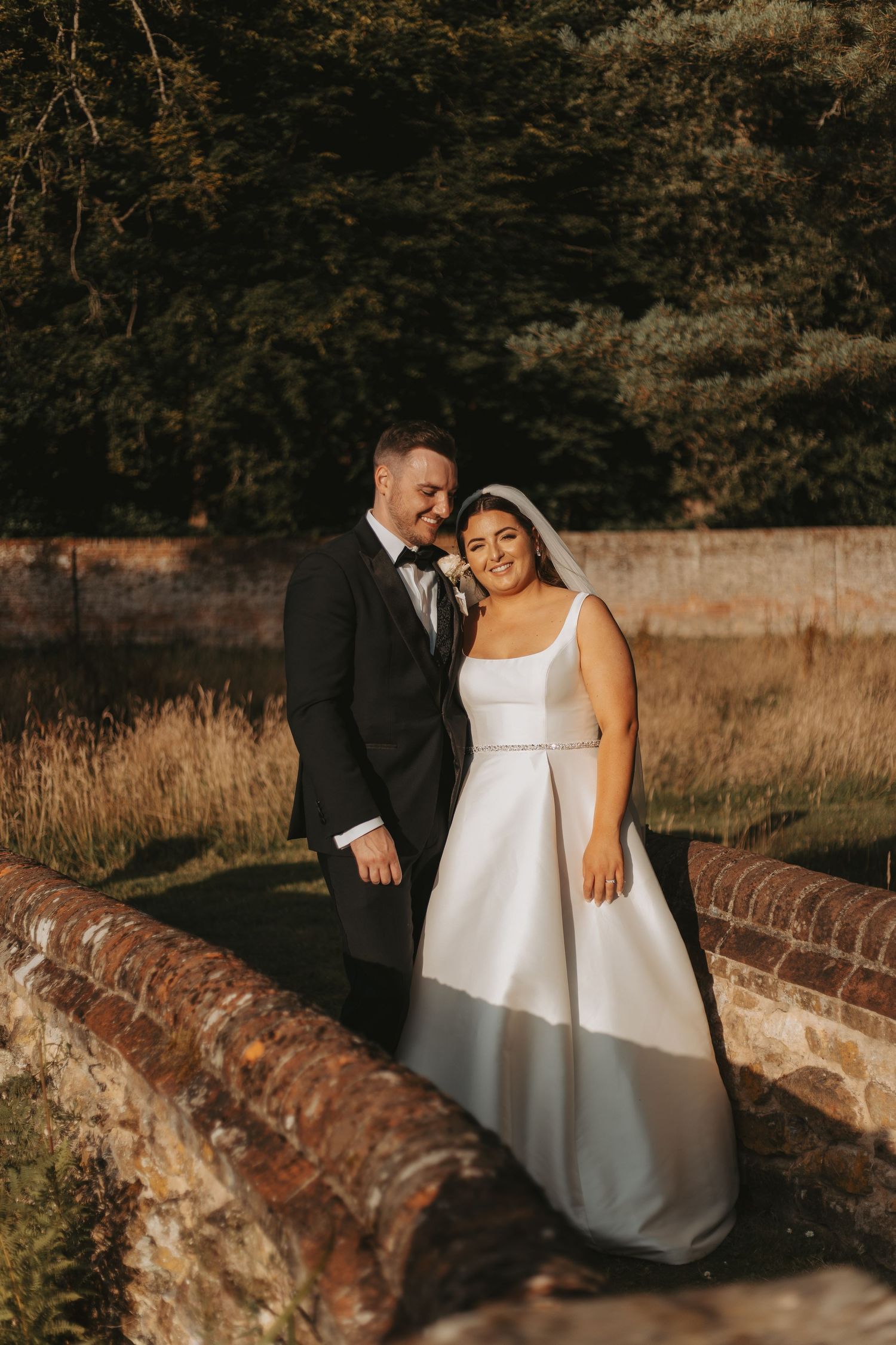Newlyweds share an intimate moment on a rustic stone wall during golden hour.