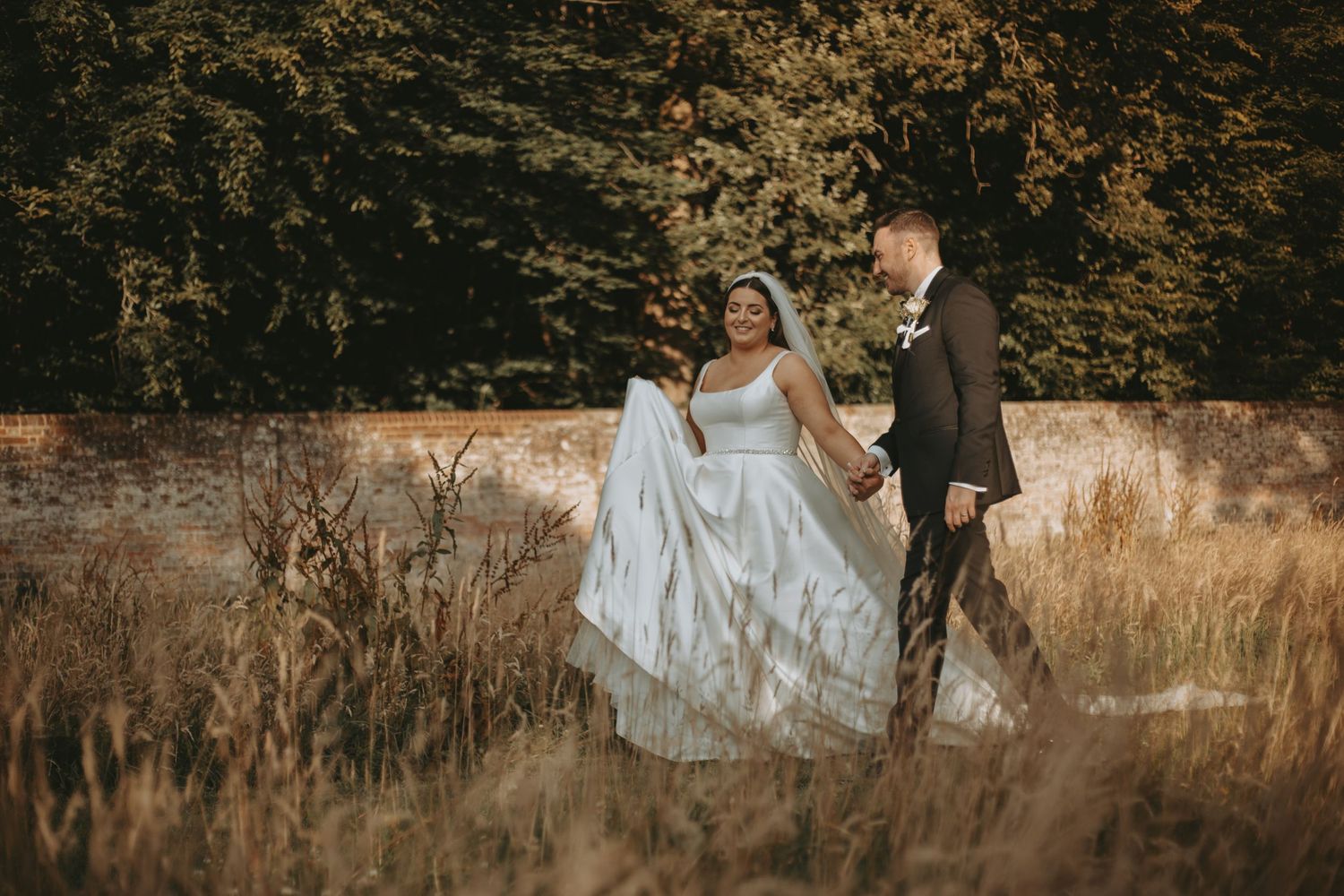 Newlyweds share intimate moment in golden sunlit field during sunset.