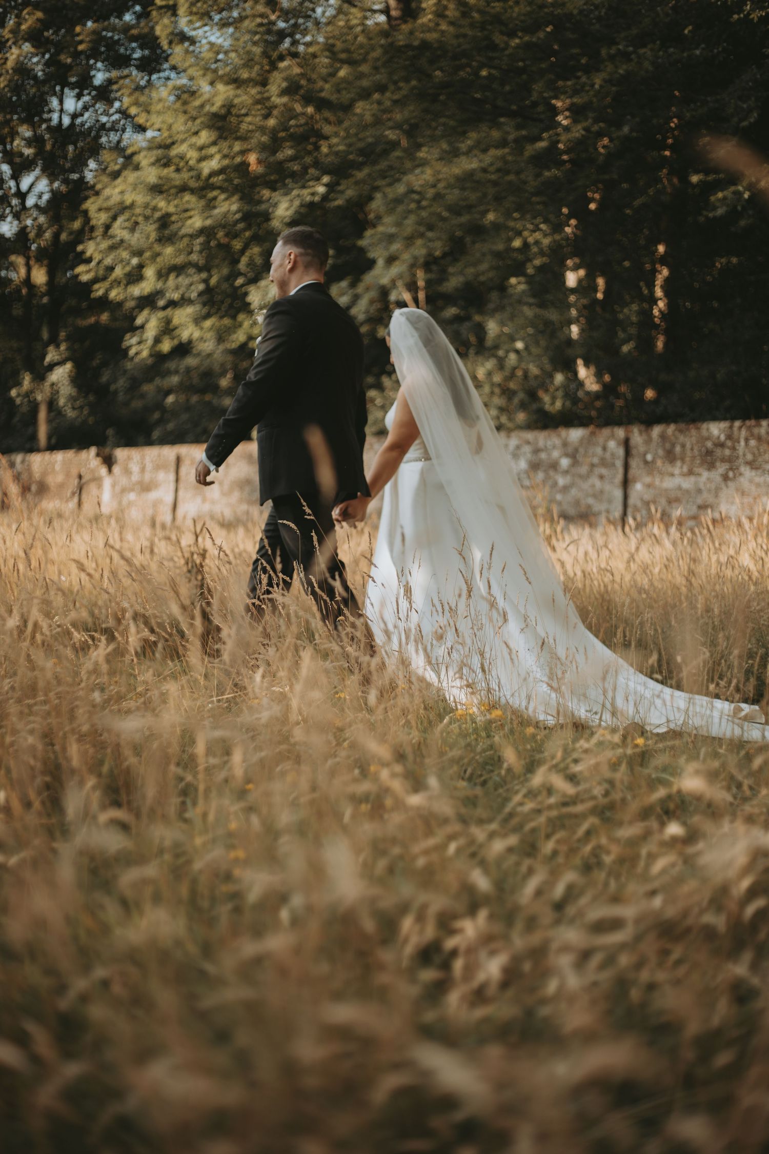 Wedding couple poses in tall golden grass during a sunset photoshoot.