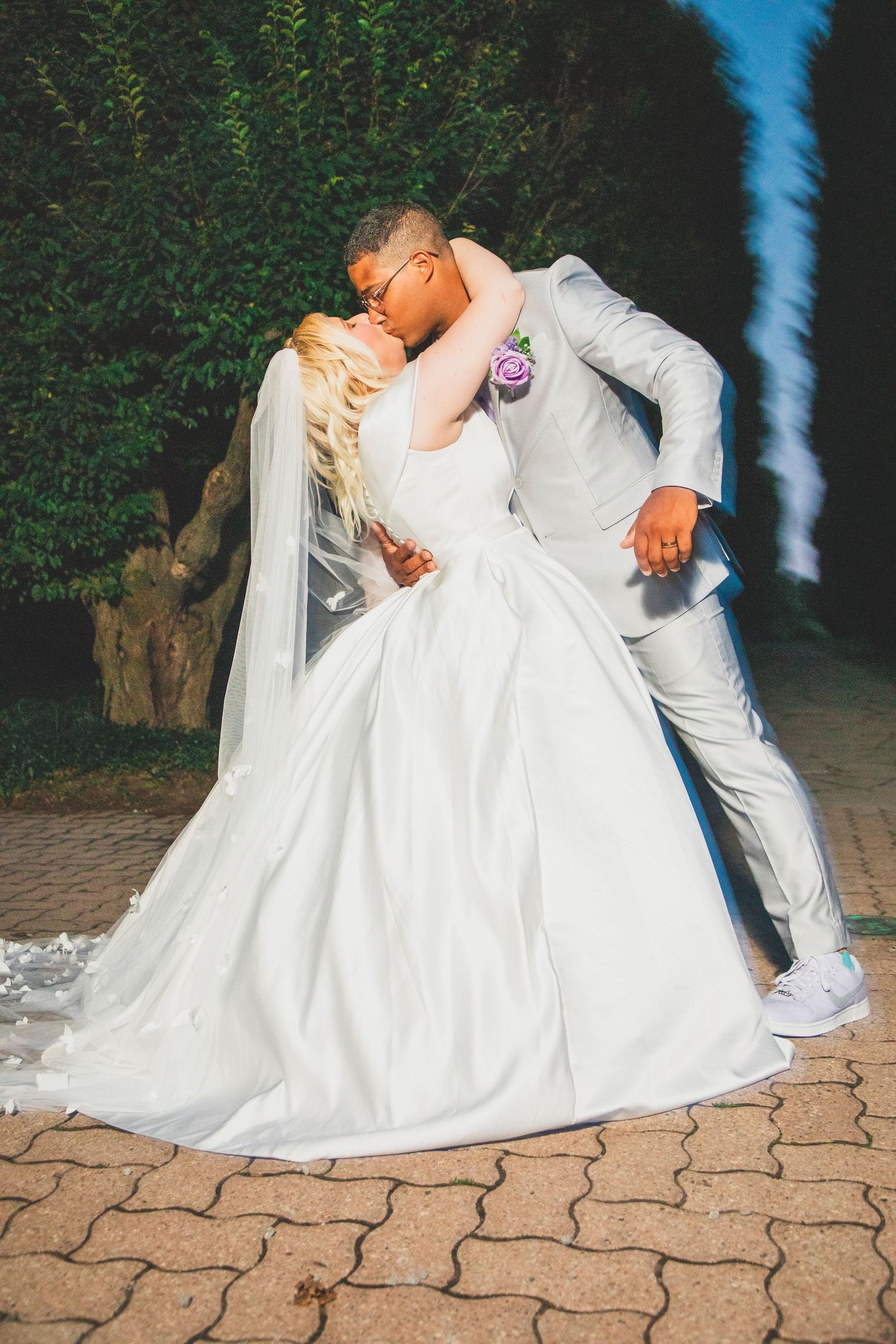 Romantic wedding photo of couple in white sharing a passionate dip kiss on brick pavers.
