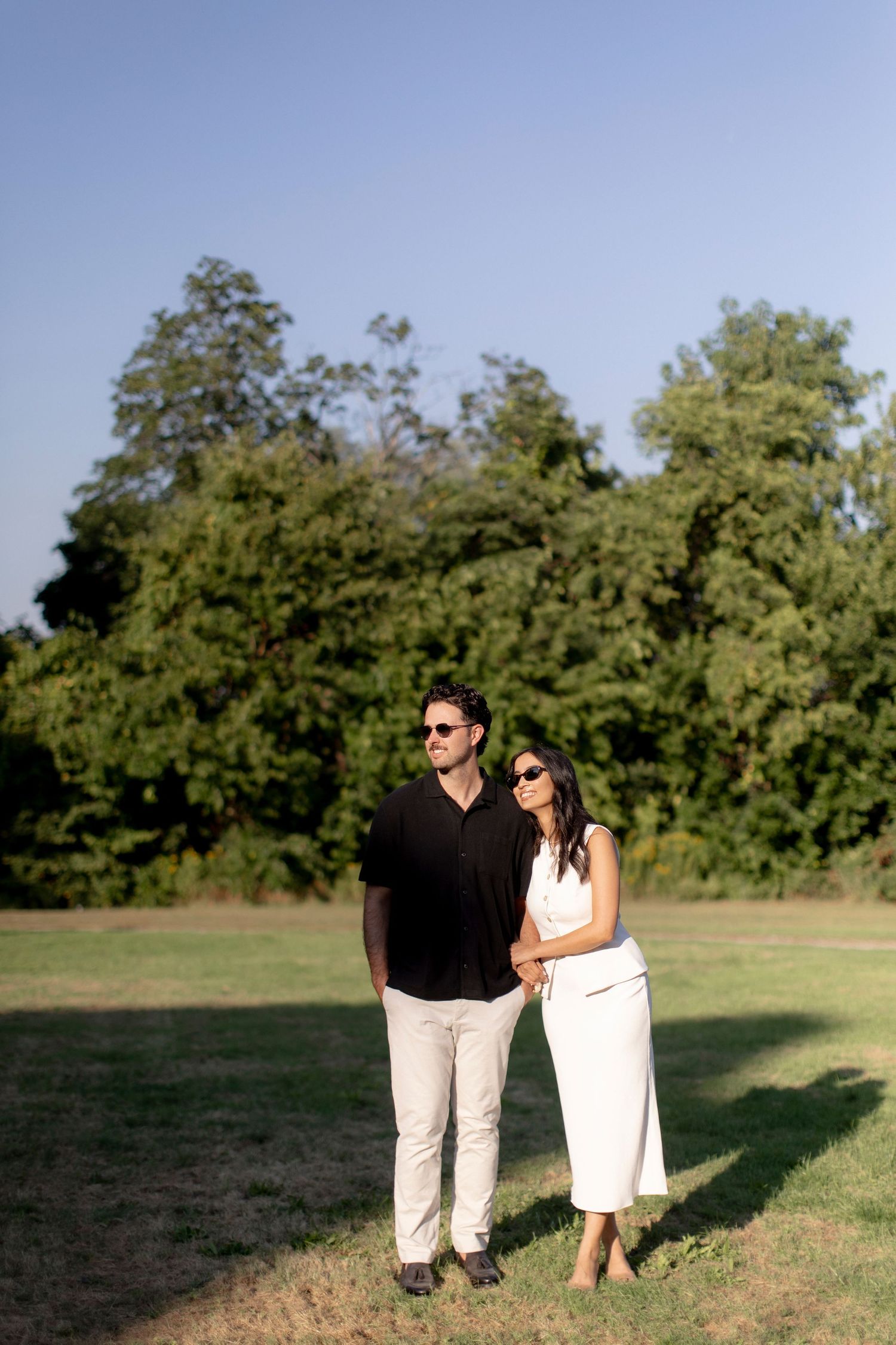 Elegant couple poses together in a garden with lush trees in the background.