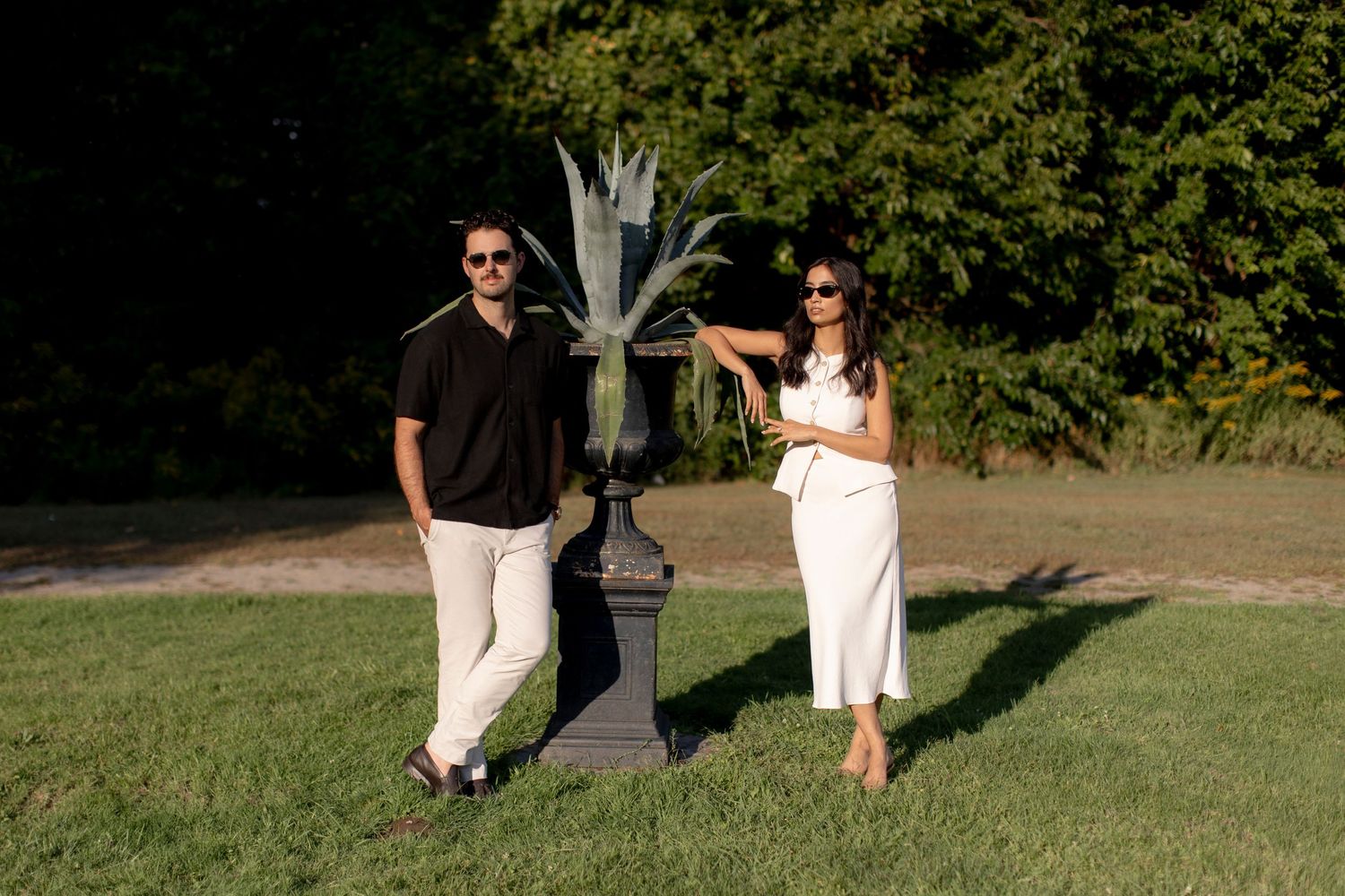 Couple in coordinated black and white outfits posing near a decorative garden urn.