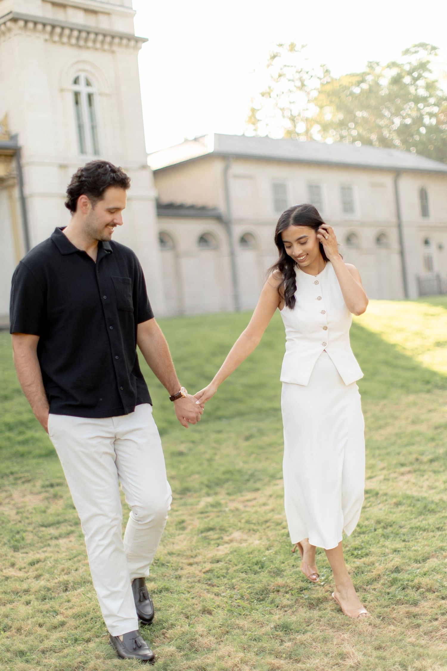 Couple holding hands while walking near a historic church building at sunset.
