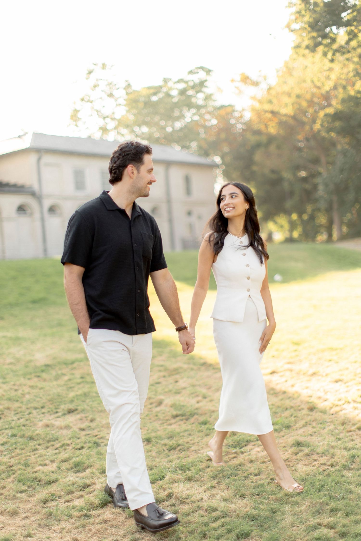 Couple strolling together on grass with church architecture in the background.