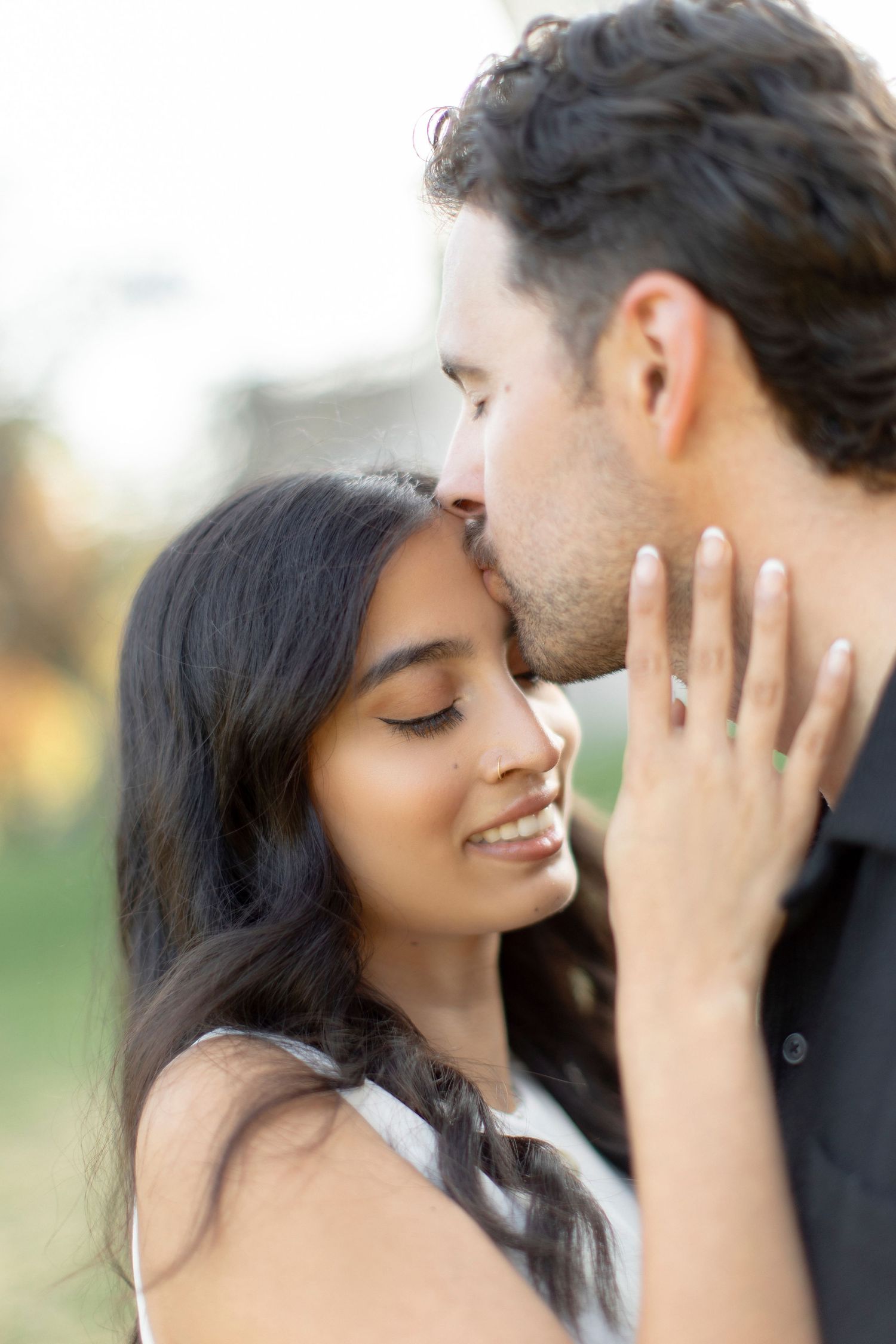 Tender close-up of a couple embracing with closed eyes against a soft background.