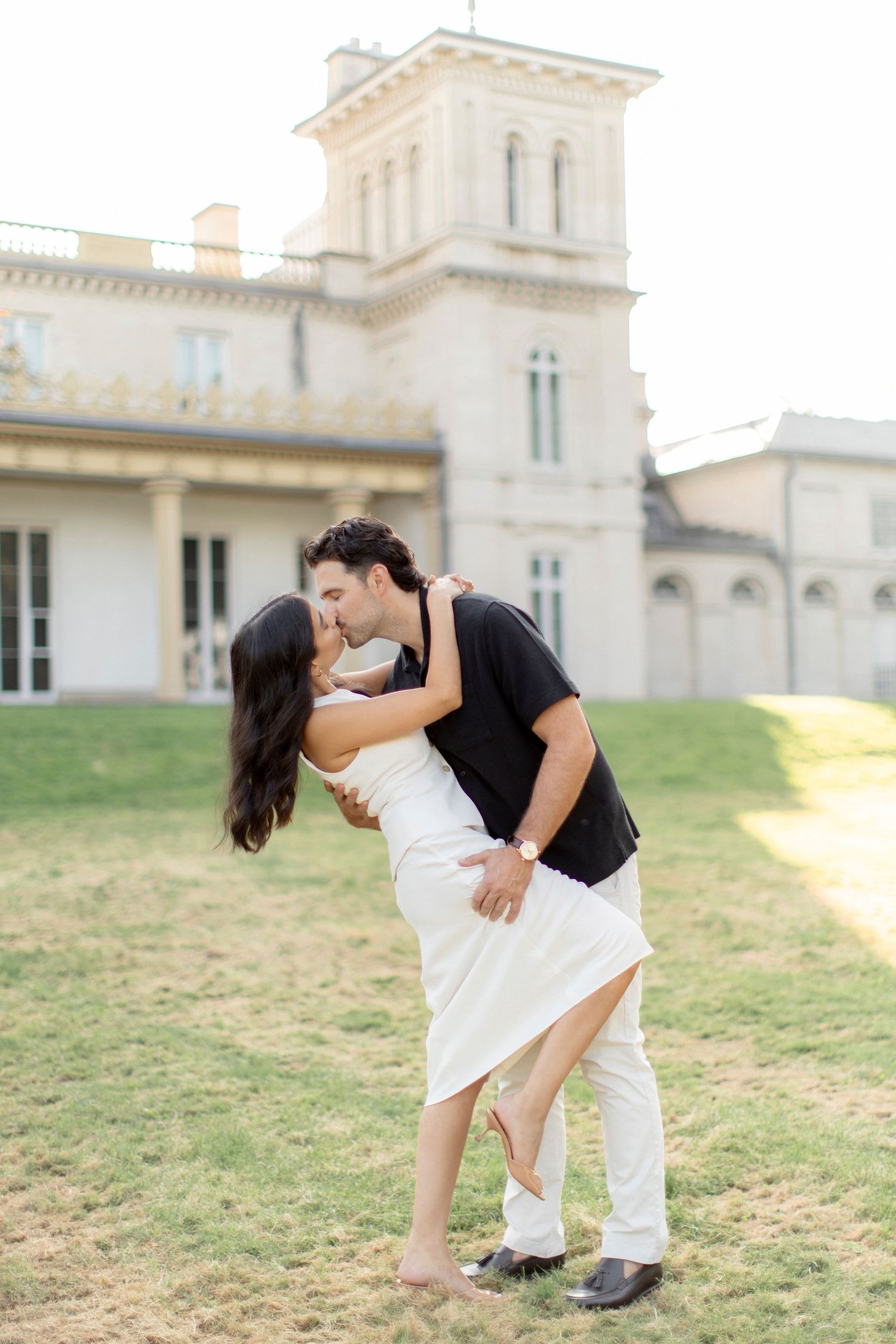 Couple in contrasting black and white outfits sharing a romantic dip pose on mansion grounds.