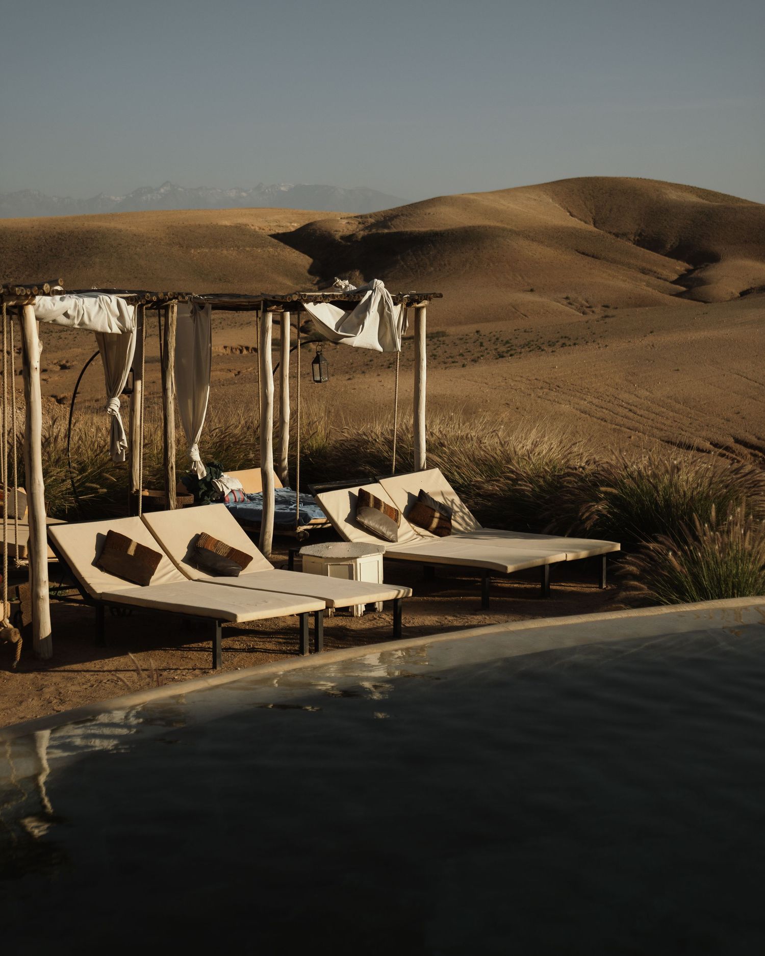 Luxury poolside lounge chairs with canopy overlooking desert sand dunes.