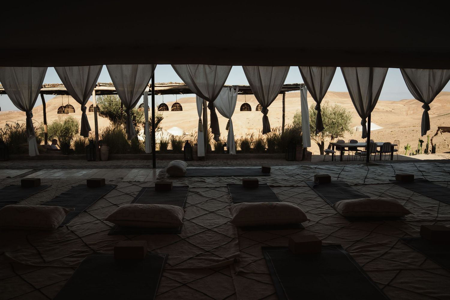 Peaceful yoga space with cushions and mats overlooking desert architecture through draped windows.