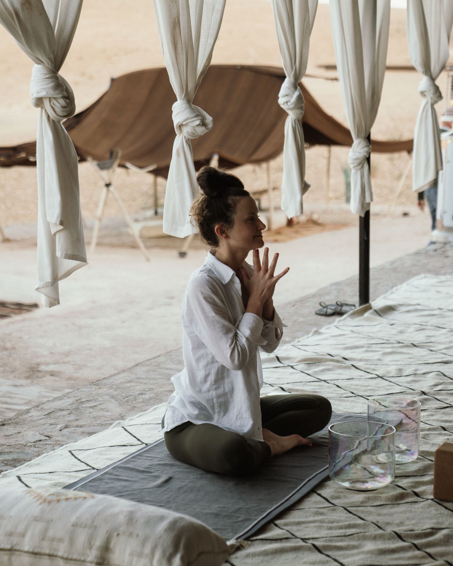 Person meditating in a serene outdoor setting with white curtains and stone floor.