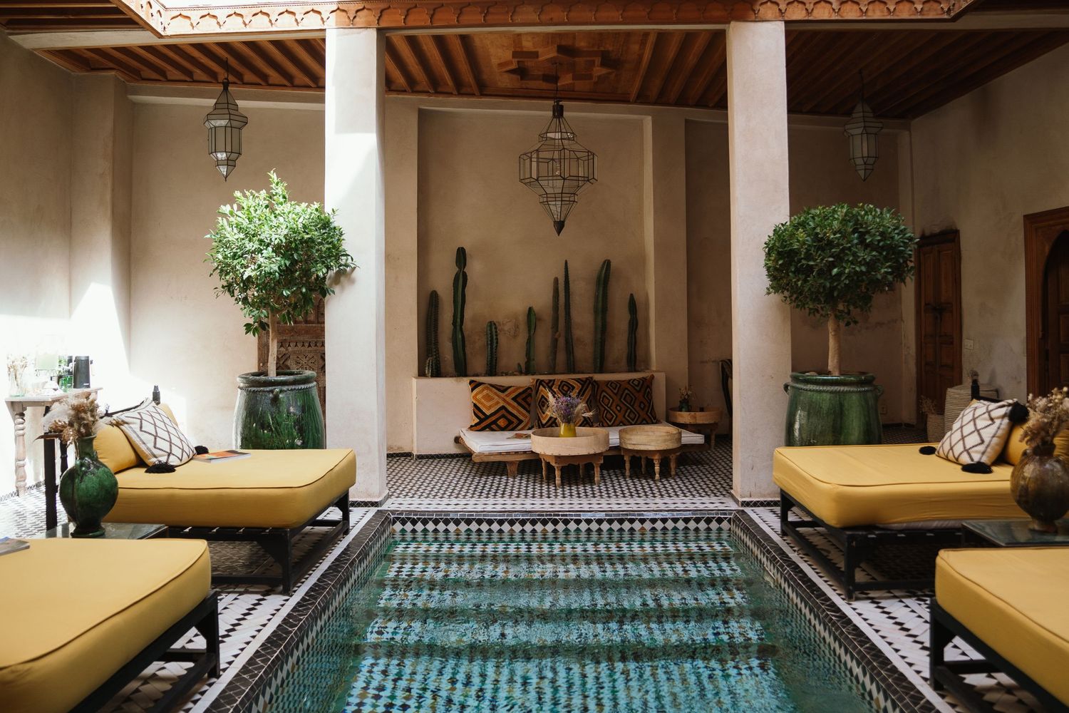 Indoor pool area with yellow daybeds and potted plants in a Moroccan-style courtyard.