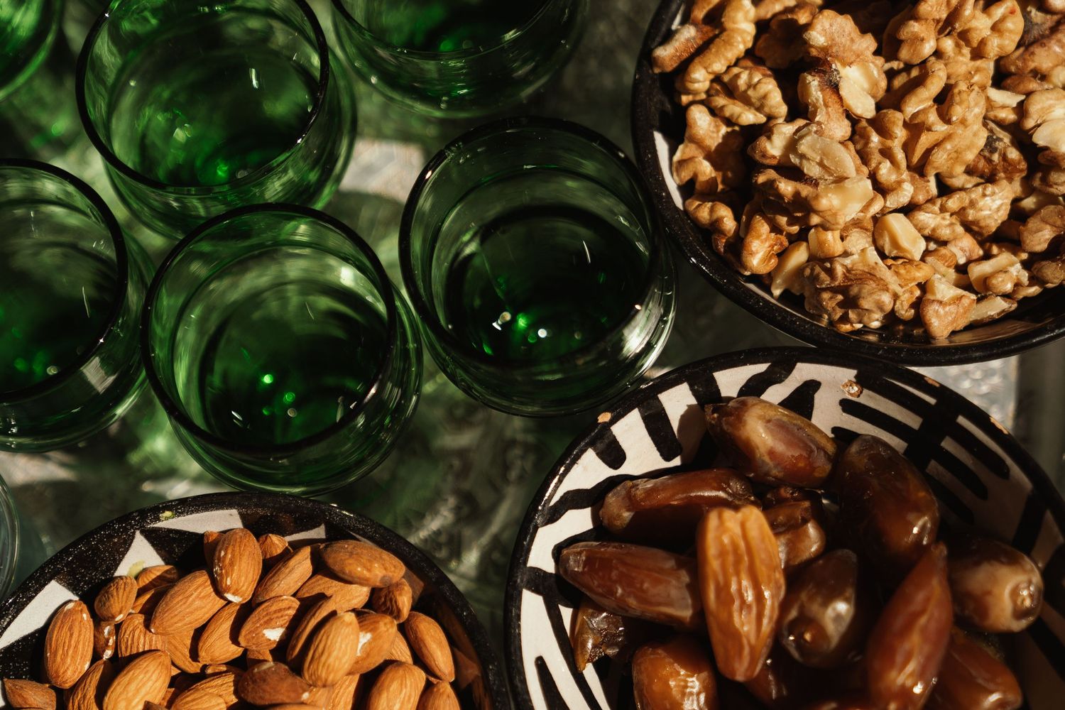 Healthy snacks including almonds, walnuts and dates arranged with green glass jars.