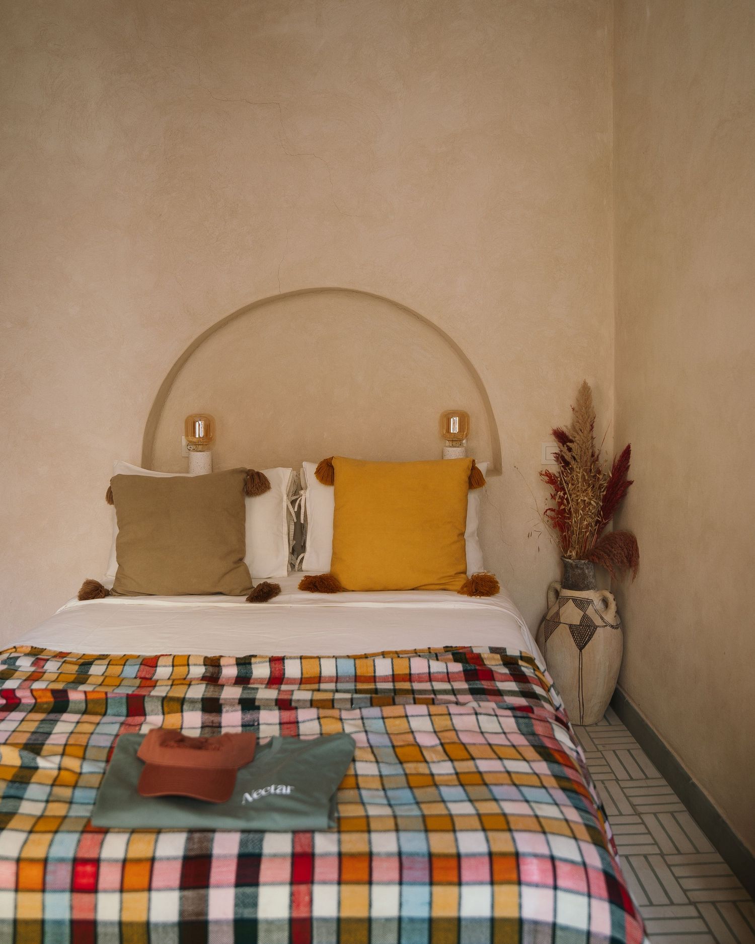 Modern bedroom featuring colorful plaid bedding, earth-toned pillows, and a curved alcove headboard.