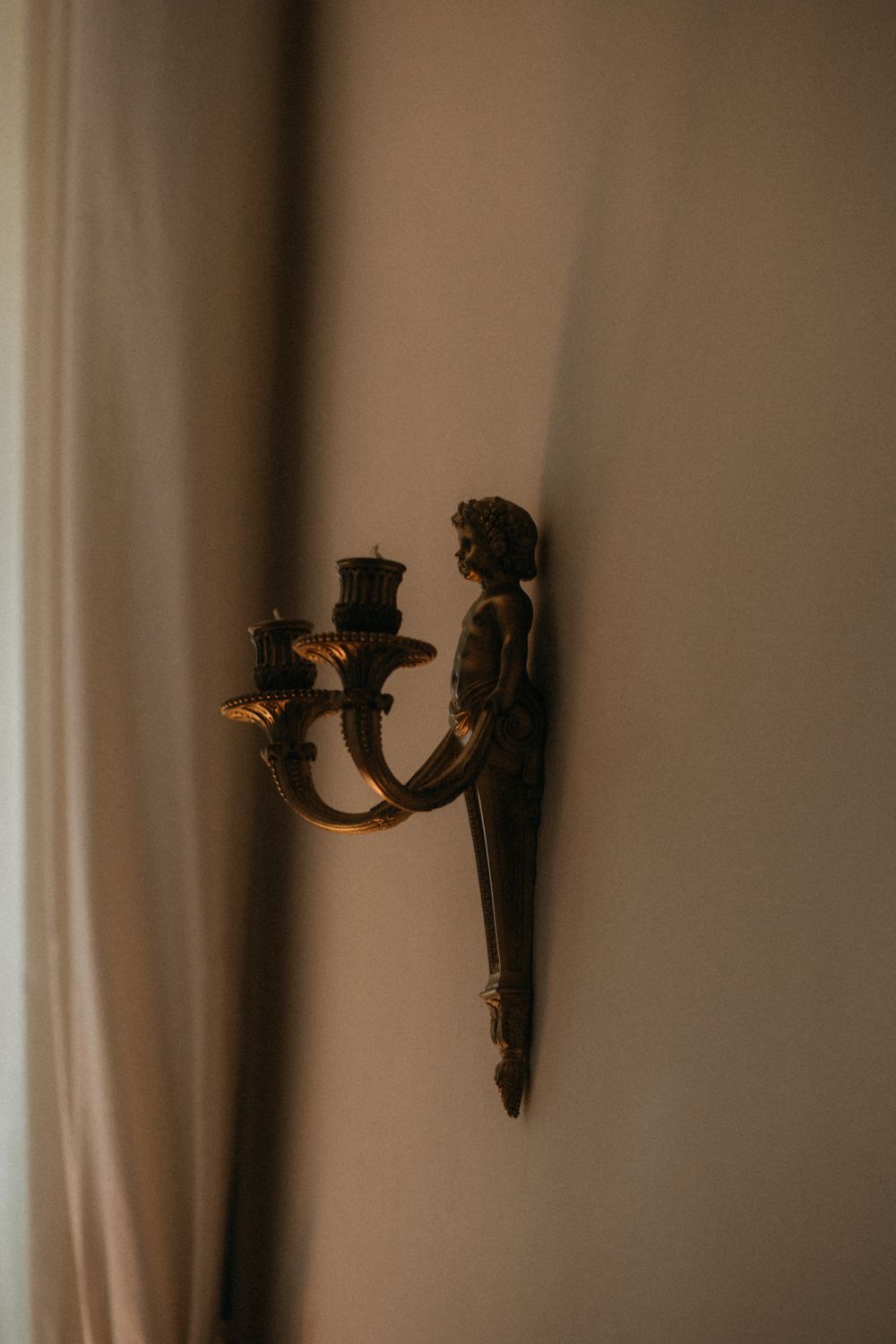 Vintage wall-mounted candelabra sconce with ornate figure detail creates moody atmospheric lighting in sepia tones.