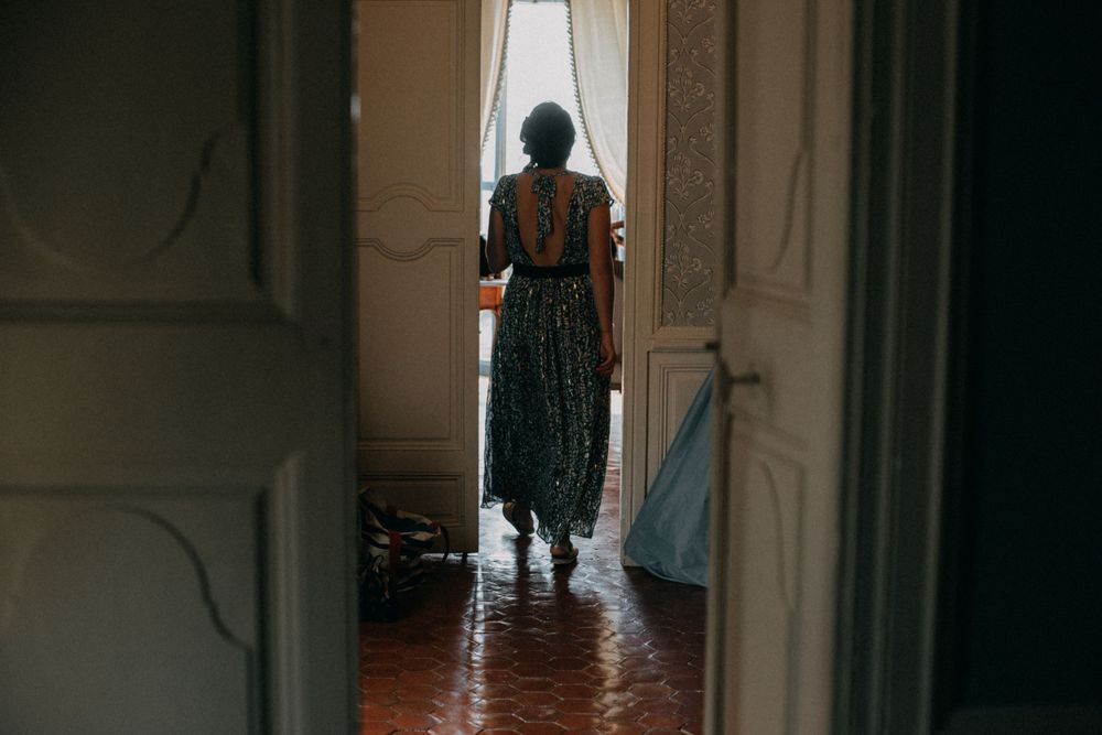 Silhouette of person in patterned dress standing by bright window in vintage interior.