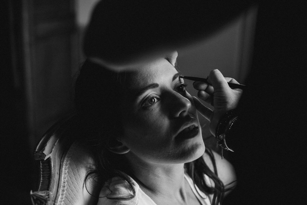 Dramatic black and white portrait with makeup application in moody lighting.