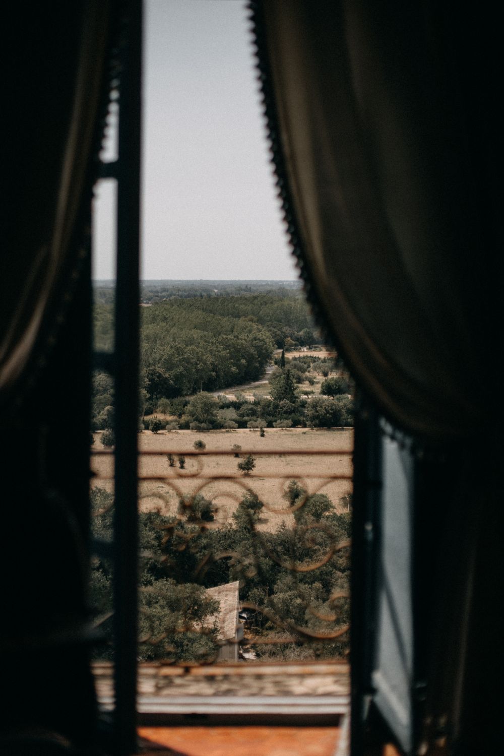 View through window curtains of a scenic countryside landscape with rolling hills and farmland.