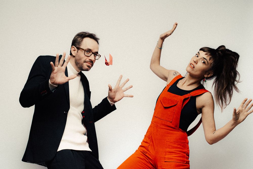 Playful studio shot of two people dancing, one wearing vibrant orange dress.
