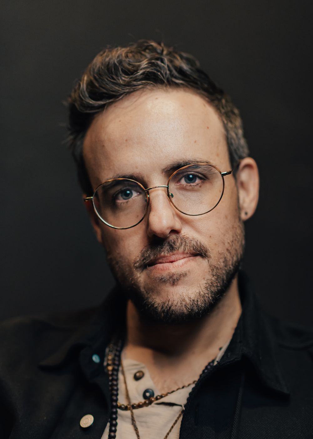 Professional headshot of person wearing glasses and black jacket.