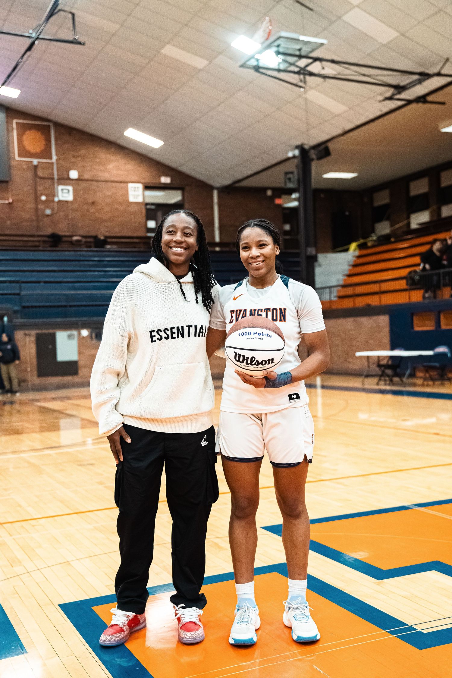 Two basketball players posing with a ball in a gymnasium setting.