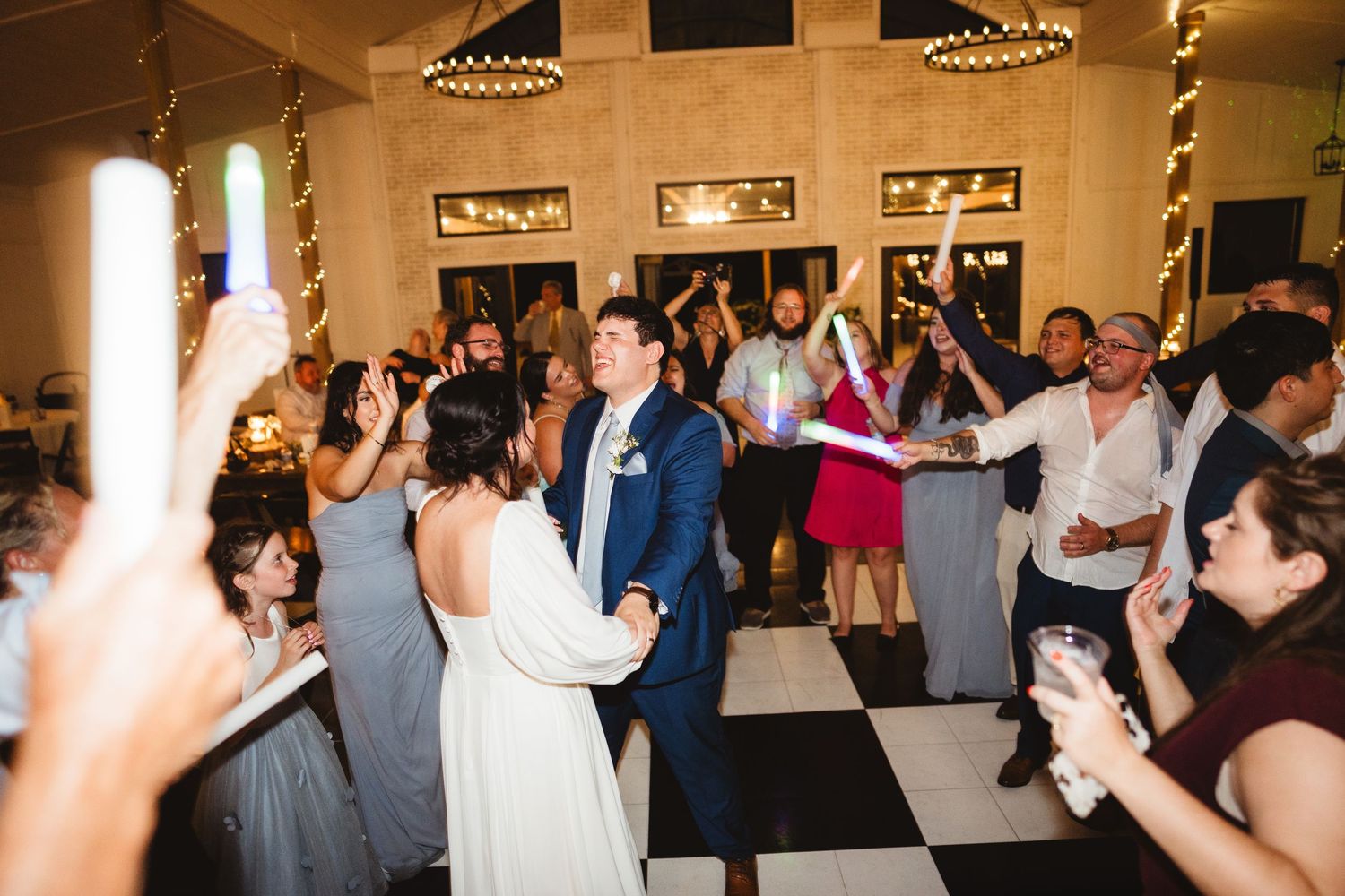 Wedding guests dance and celebrate on a black and white checkered dance floor at a reception venue.