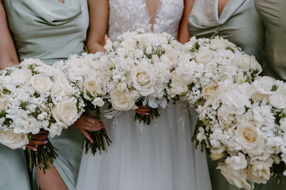 Row of bridesmaids in sage green dresses holding elegant white floral bouquets at formal wedding ceremony.