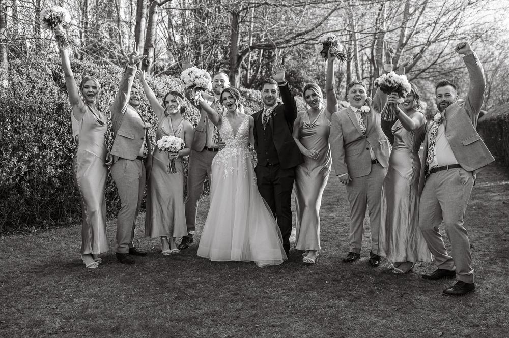 Wedding party poses together outdoors in winter setting with bare trees and mauve grey bridesmaid gowns.