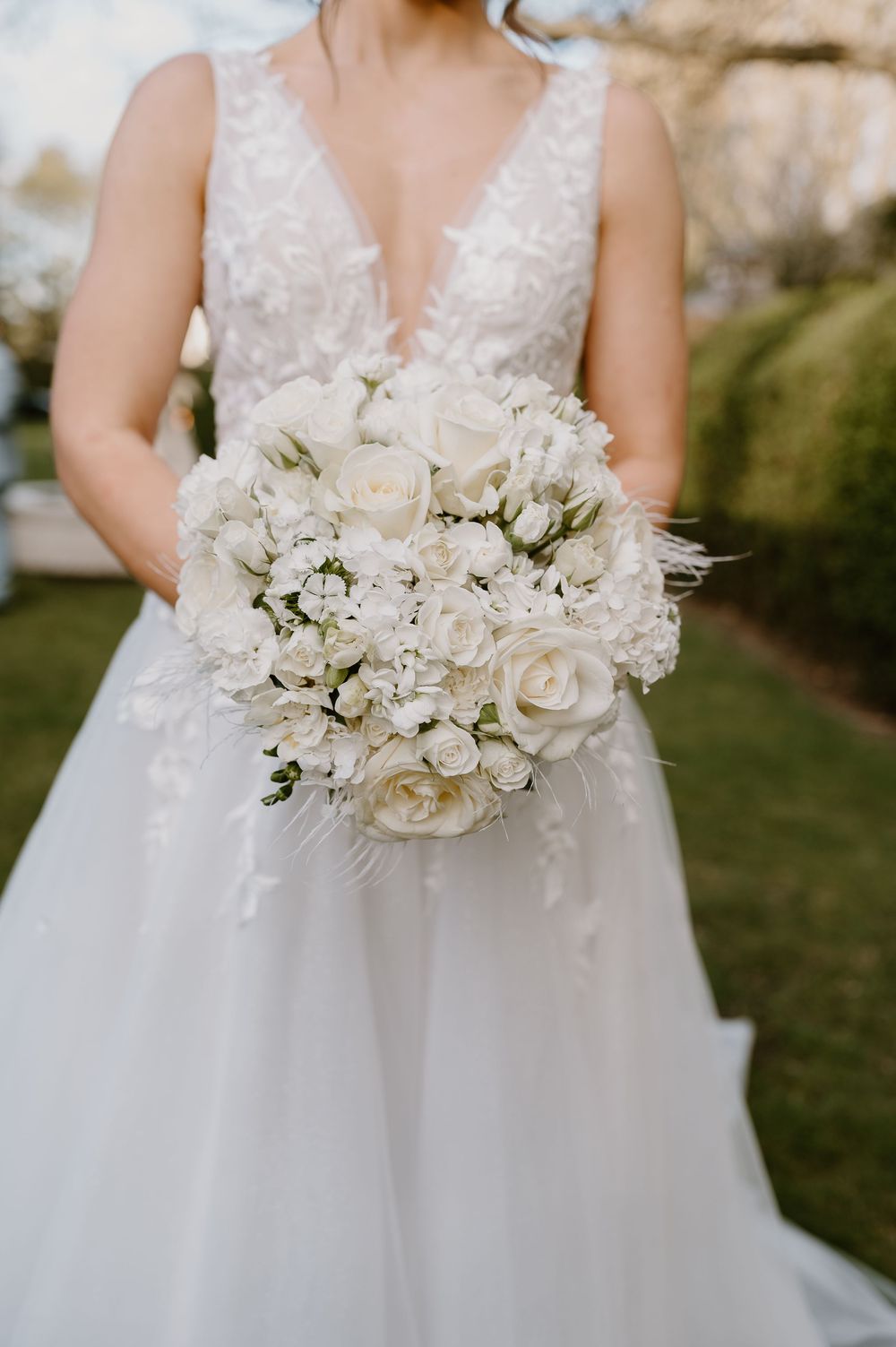 Close-up of a white wedding dress and bouquet featuring white roses and delicate flowers.