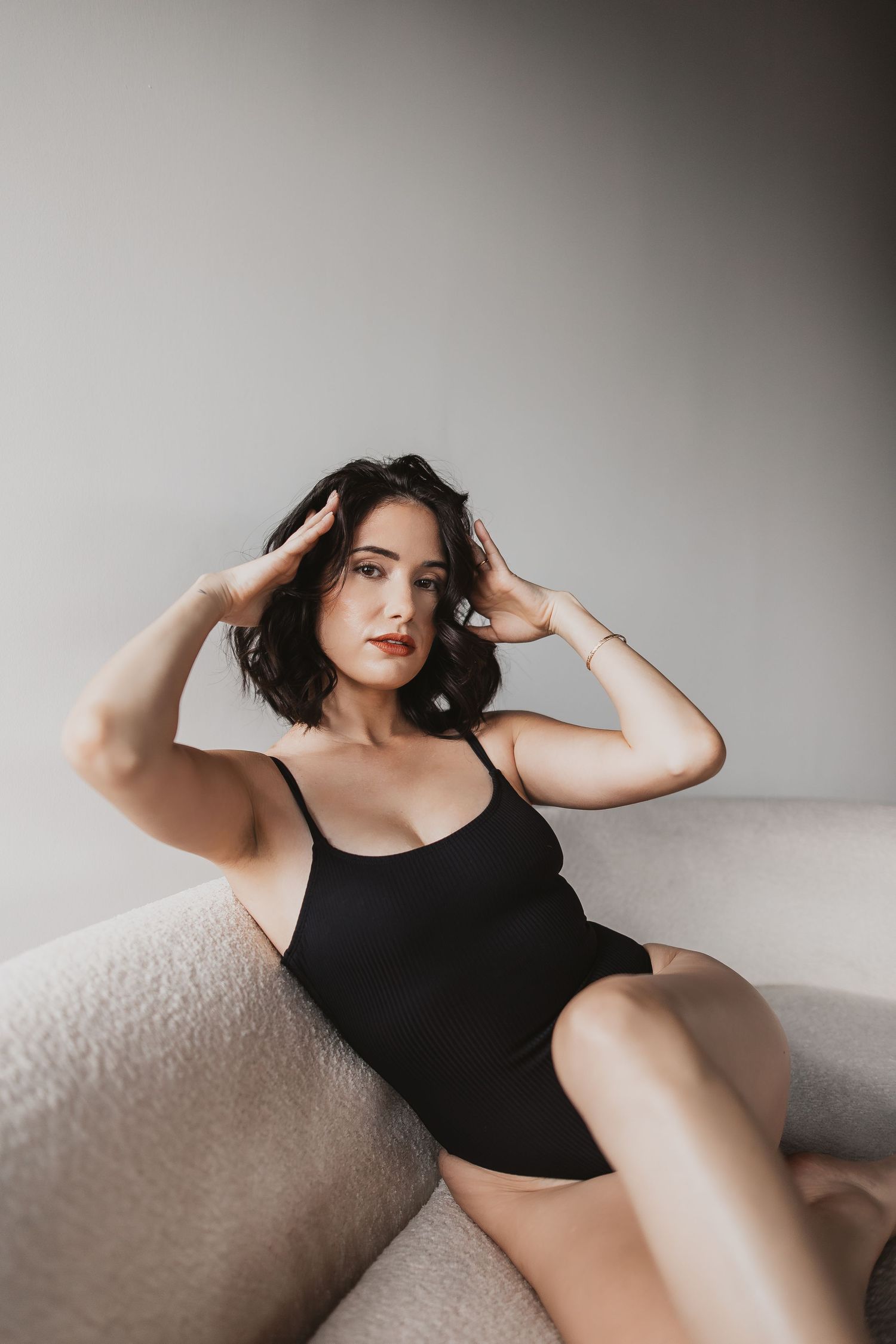 Minimalist portrait of person in black bodysuit posing on light colored couch.