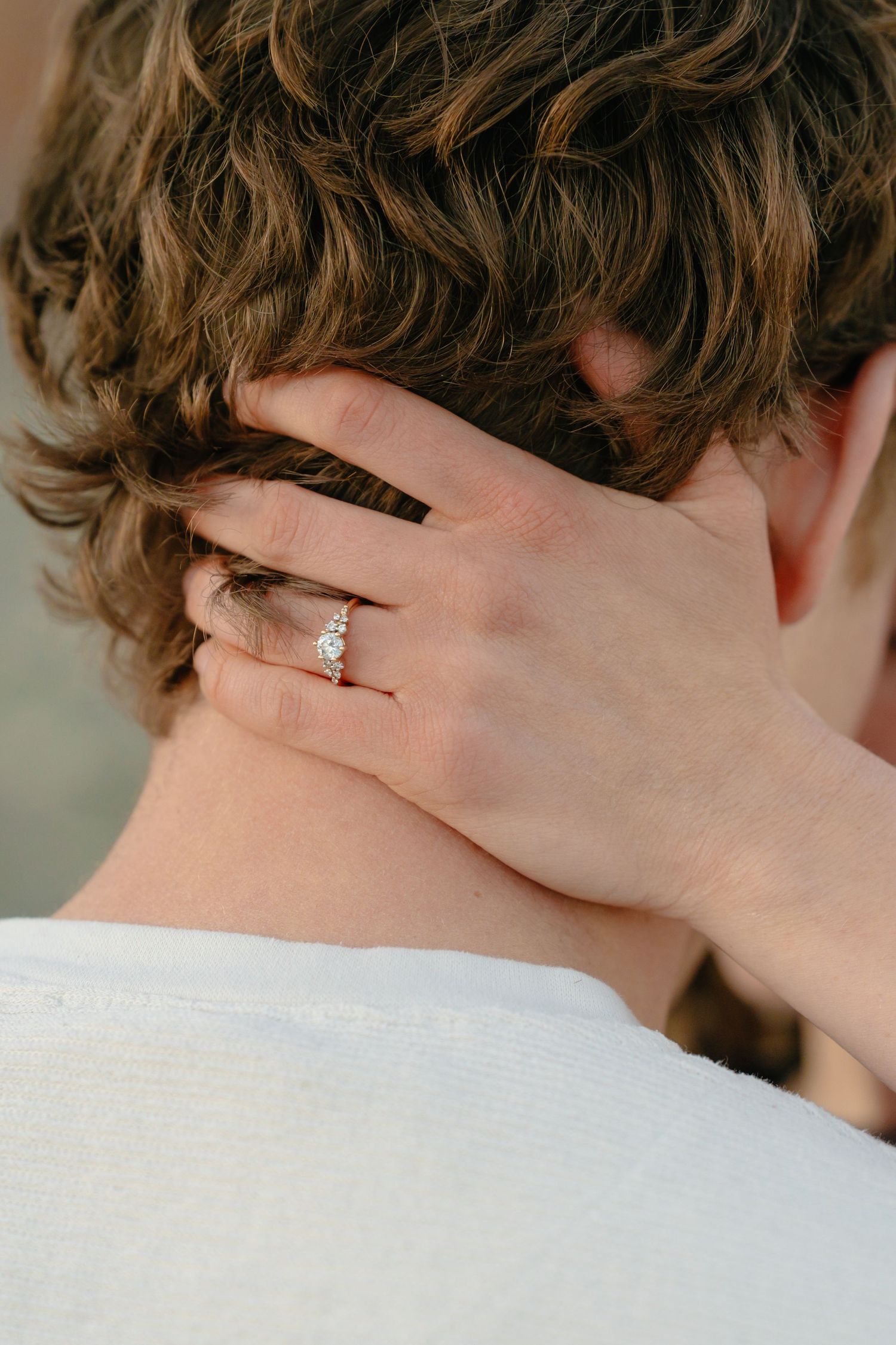 Des Moines engagement photography detail: bride touching groom's neck with wedding ring in soft light