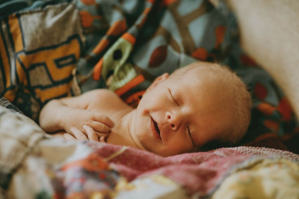 A sleeping baby rests peacefully on colorful blankets with a soft glow across their face.
