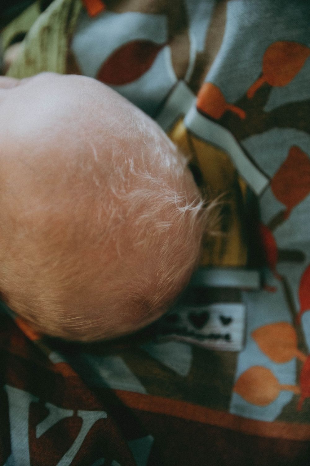 A close-up view of a baby's fuzzy head against colorful patterned fabric.