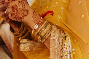 Ornate henna design and golden bangles adorned with sparkles against yellow fabric in traditional Indian wedding attire.