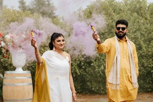Group celebrates outdoor wedding ceremony with colorful smoke bombs in yellow and pink.
