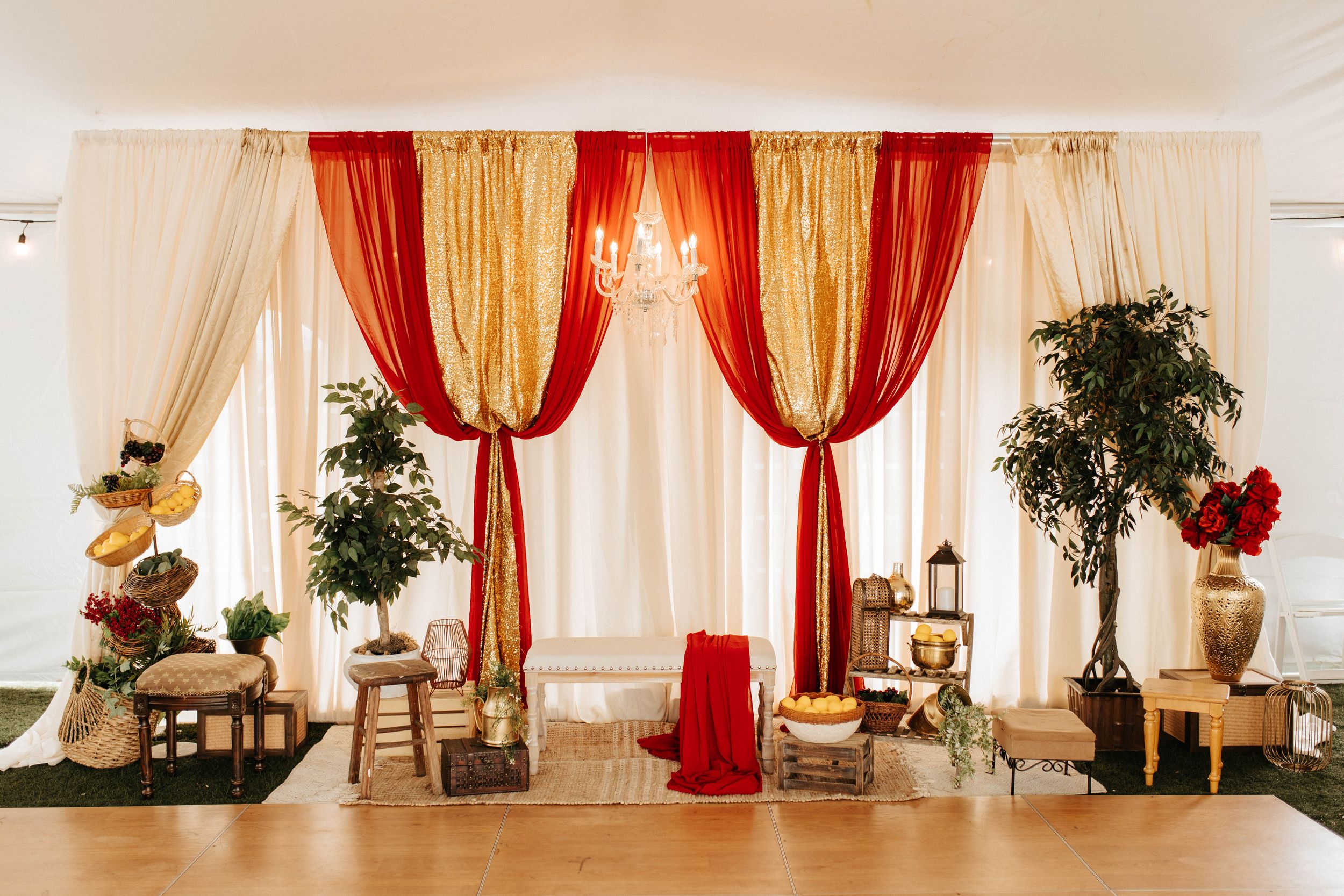 Elegant event setup with red and gold draped curtains, chandelier, and decorative plants.