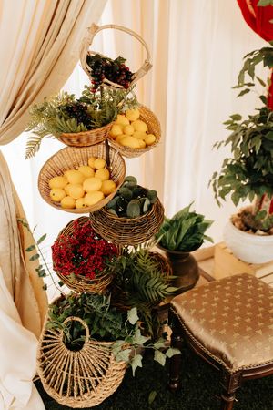 Three-tiered gold metal display stand decorated with greenery, berries and yellow fruit on a pale beige background.