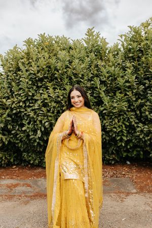 Beautiful yellow traditional Indian lehenga outfit photographed against a green hedge backdrop in outdoor setting.