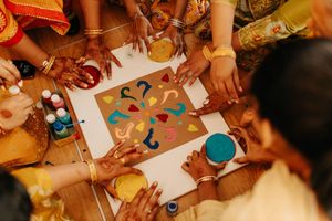 Traditional Indian art creation with colorful powders and hands reaching in to collaborate on the design.