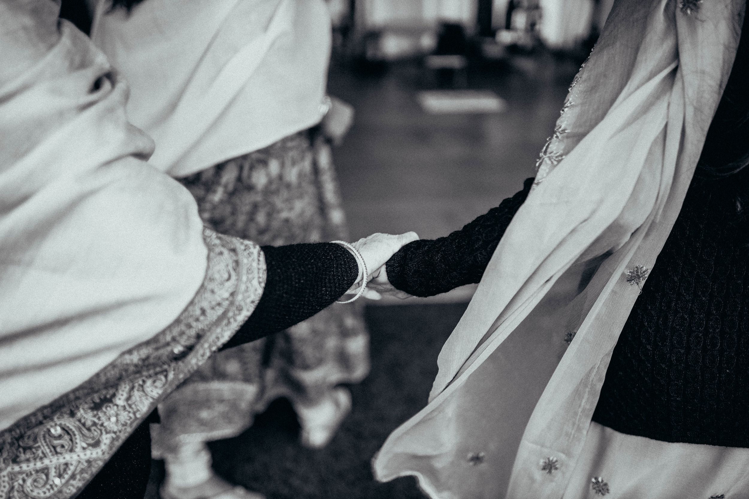 Black and white close-up shot of hands holding traditional wedding attire with intricate details.