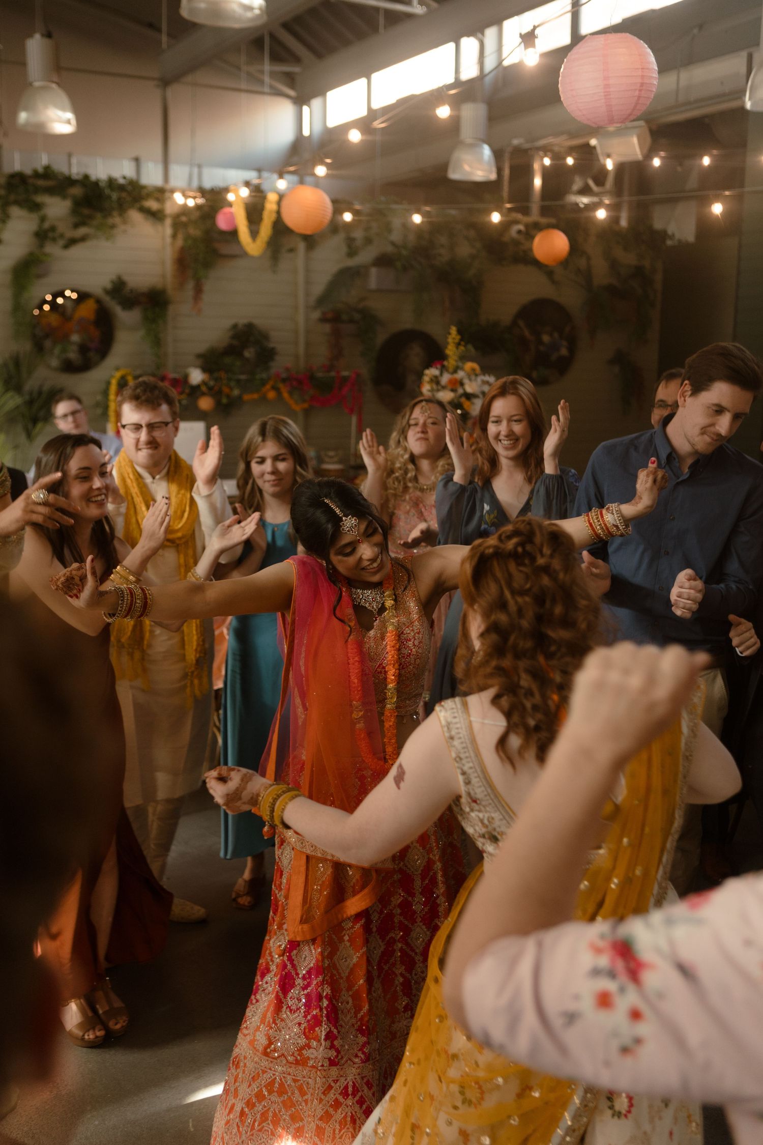 Wedding reception guests dancing and celebrating on a dance floor under string lights and paper lanterns.