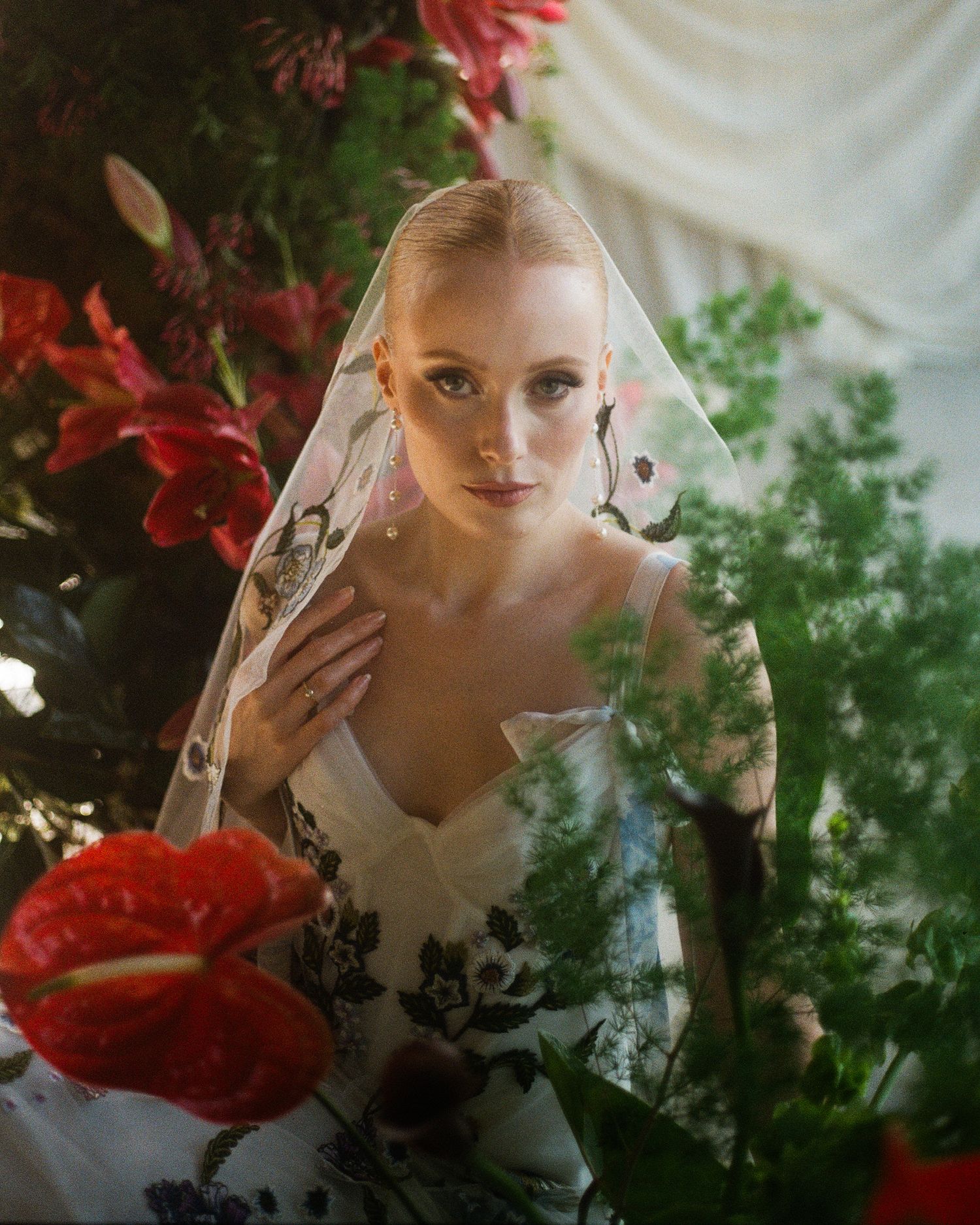 A dreamy portrait through sheer fabric with red flowers creating an ethereal artistic effect.